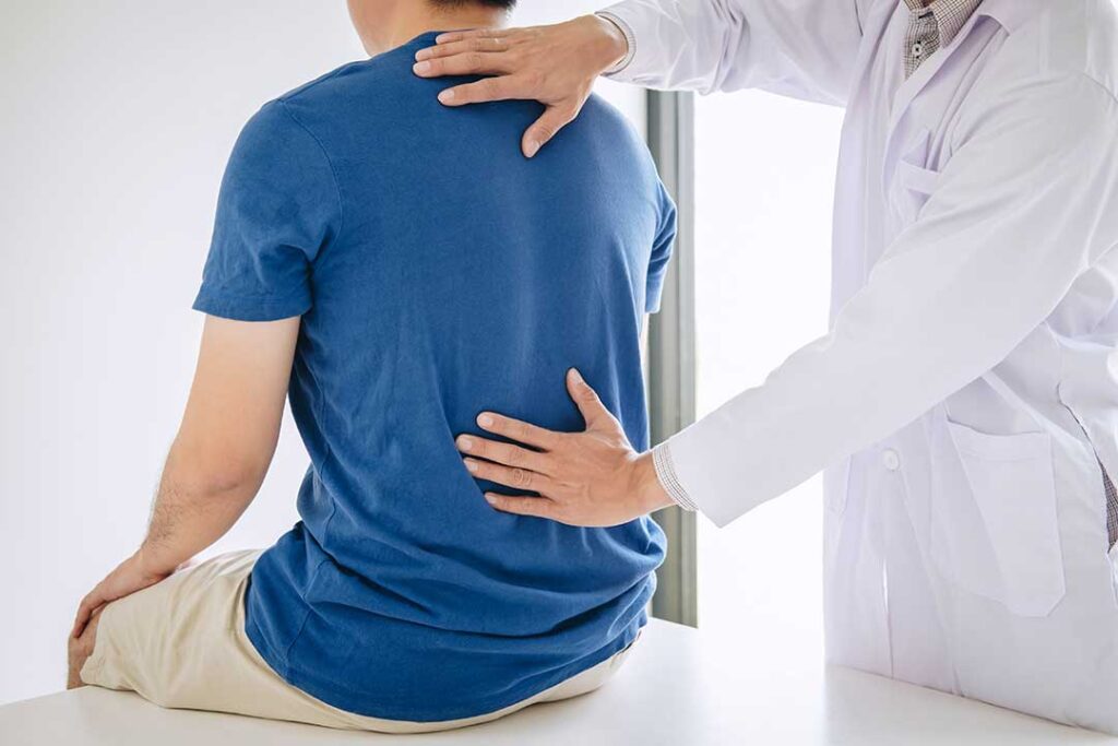 Adult performing gentle shoulder and neck mobility exercises beside a chair in a bright home.